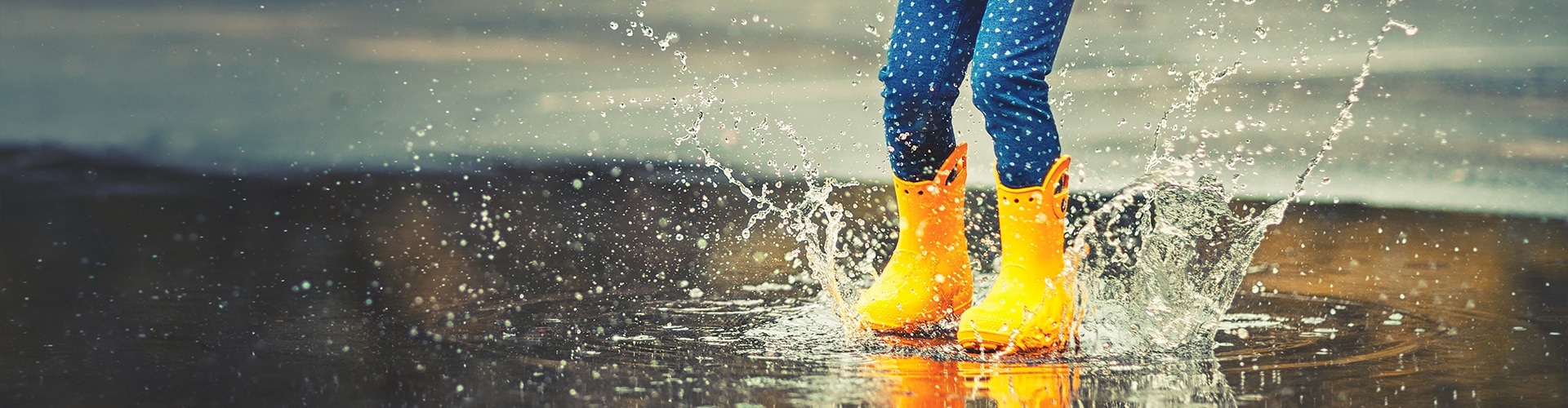 Kind in gelben Gummistiefeln springt in eine Pfütze – Kinderorthopädie bei Gangauf